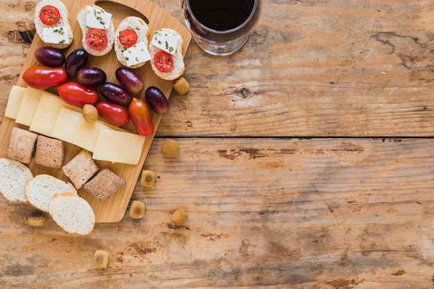 Grapes, tomatoes, cheese slices, bread and pastries with wineglass on wooden desk