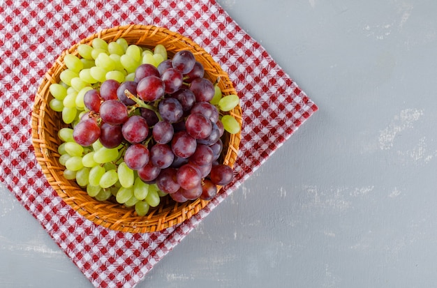 Foto gratuita uva in un cesto di vimini su stoffa da picnic e intonaco,