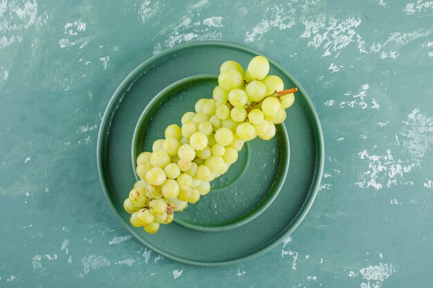 Grapes with plate in a saucer on plaster background, flat lay.