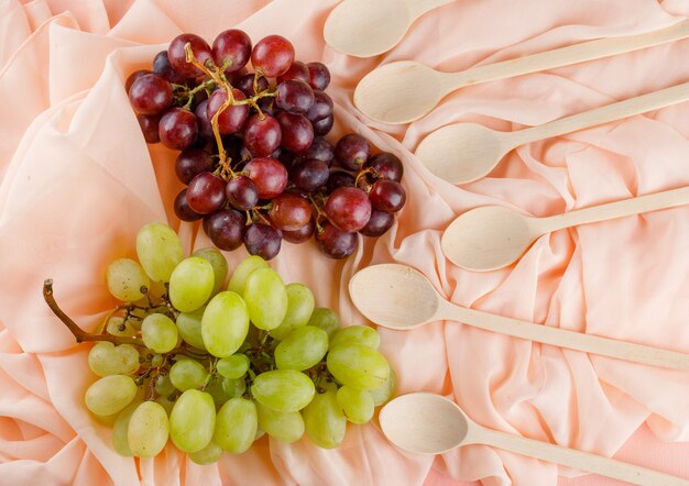 Grapes with wooden spoons flat lay on a pink textile