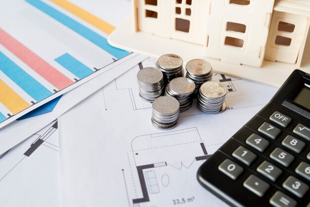 Graph; stack of coins; calculator and house model on blueprint