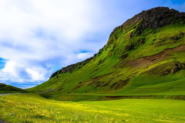 Grassy Field Near a Grass Mountain Under a Cloudy Sky – Free Stock Photo