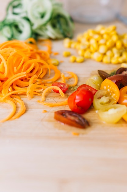 Grated carrot; corn seeds and slices of cherry tomatoes on wooden background