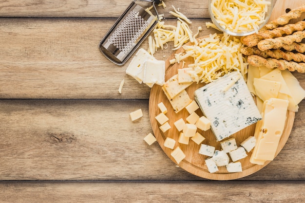 Free photo grated cheese, cheese blocks and bread sticks over the desk