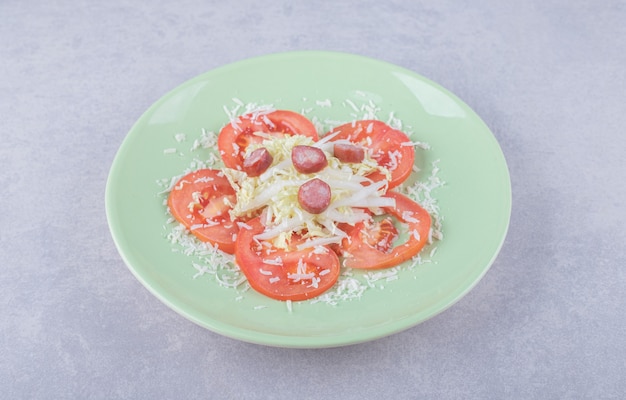 Free photo grated cheese with sausages and tomato on green plate.