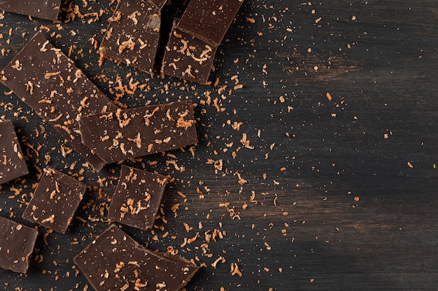 Grated chocolate with choco bars on dark background, flat lay.