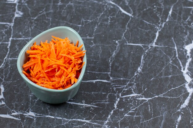 Grated fresh carrot in a blue ceramic bowl.