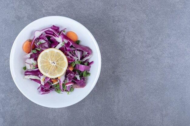 Grated vegetables with lemon on the plate, on the marble background.