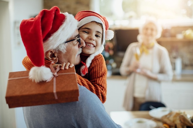 Grateful little girl embracing her grandfather while receiving Christmas present from him