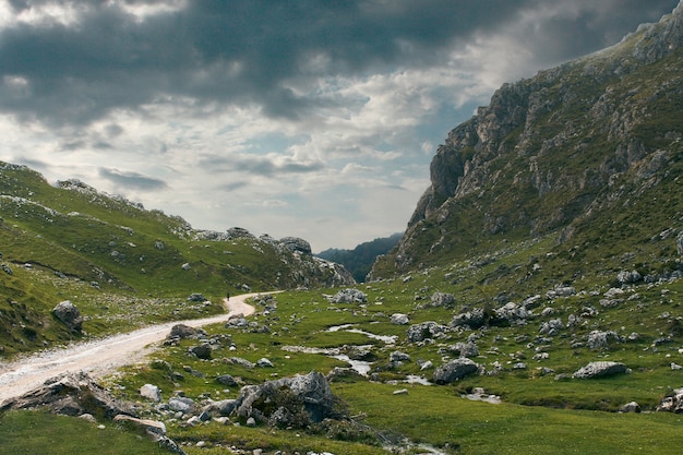 Gravel road surrounded by grass-covered lands and mountains on a cloudy day