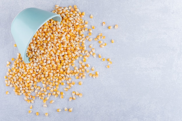 Gray bowl pouring out corn kernels on marble surface