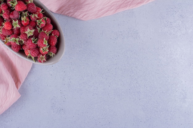 Free photo gray bowl stocked with raspberries on marble background. high quality photo