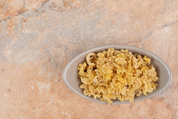 A gray bowl of unprepared macaroni on marble background. High quality photo