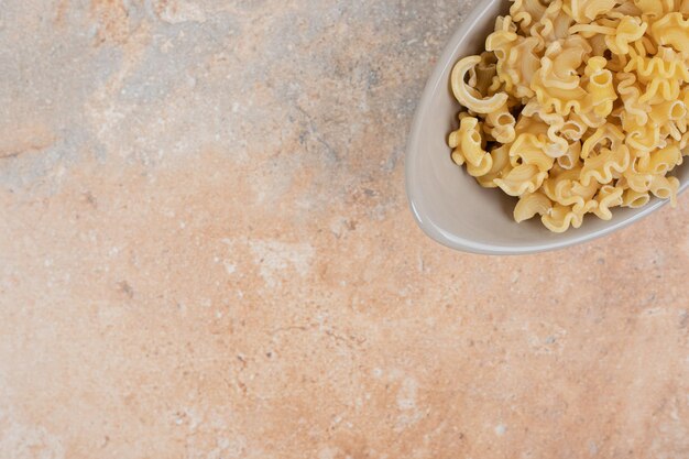 A gray bowl of unprepared macaroni on marble space. 