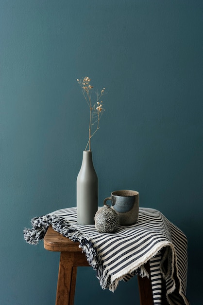 Gray ceramic vase with a mug on a wooden stool by a forest green wall