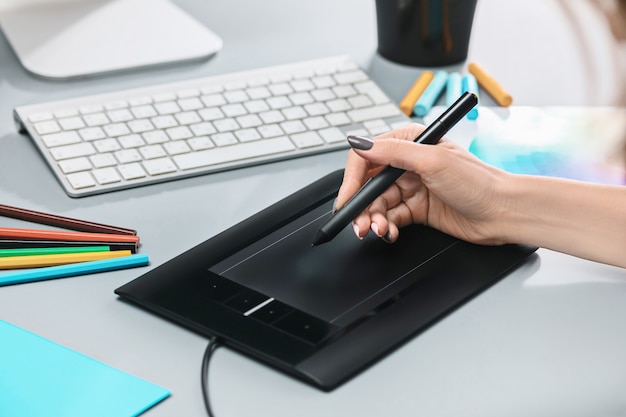 gray desk with laptop, notepad with blank sheet, pot of flower, stylus and tablet for retouching