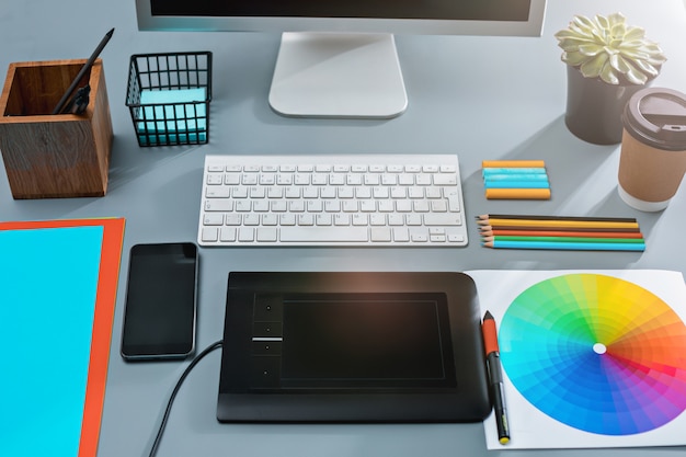 Free photo gray desk with laptop, notepad with blank sheet, pot of flower, stylus and tablet for retouching