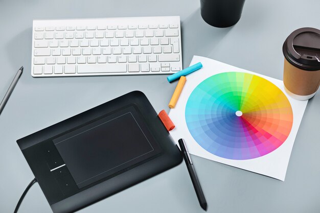 The gray desk with laptop, notepad with blank sheet, pot of flower, stylus and tablet for retouching