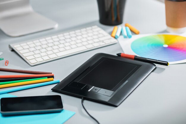 노트북이있는 회색 책상, 빈 시트가있는 메모장, 꽃 냄비, 스타일러스 및 태블릿