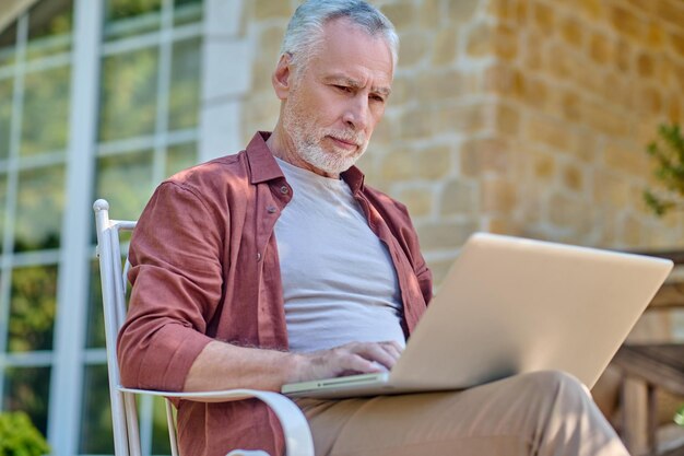 肘掛け椅子に座ってオンラインで何かを読んでいる白髪の男