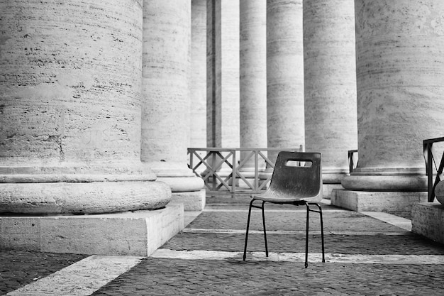 Gray scale shot of an abandoned plastic chair in a building with columns in Rome