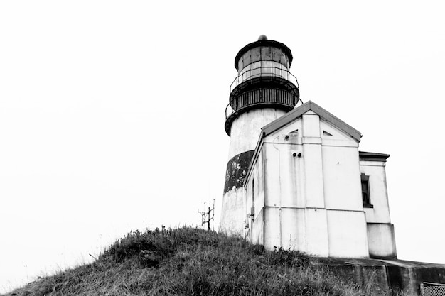 Free photo grayscale low angle shot of a lighthouse near a small cabin on a cliff