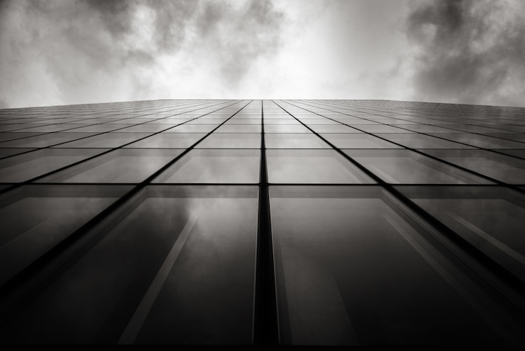 Free Photo grayscale low angle shot of a skyscraper a wall with glass windows under the cloudy sky