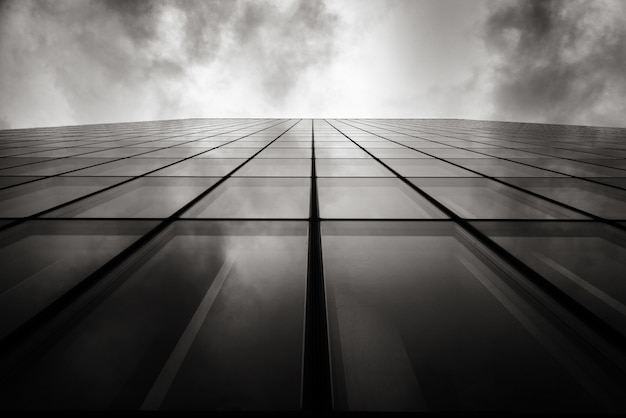 Grayscale low angle shot of a skyscraper a wall with glass windows under the cloudy sky