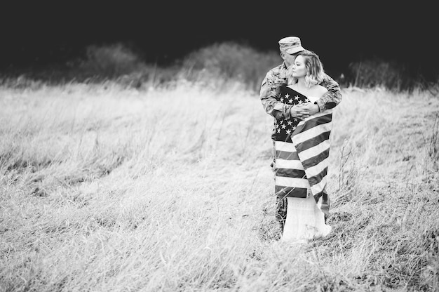 彼女がアメリカの国旗に包まれている間、彼の妻を抱き締めるアメリカの兵士のグレースケールショット