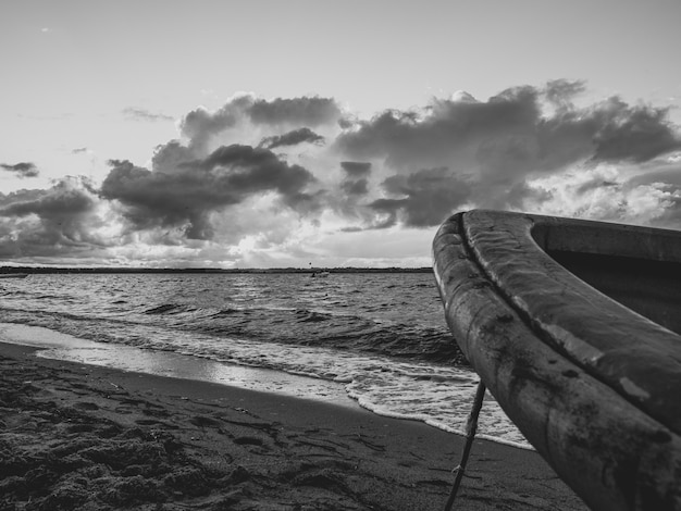 Grayscale shot of a boat front on a beach with large waves