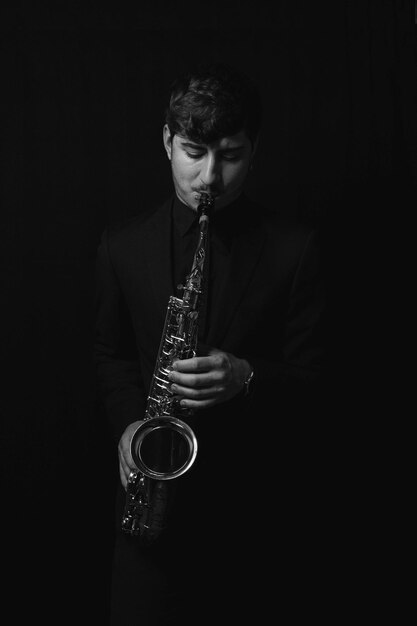 Снимок в оттенках серого крутого и красивого парня, играющего на саксофоне на темном фоне