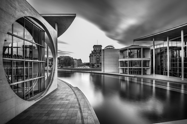 Foto gratuita scatto in scala di grigi di un lago nel mezzo degli edifici della città sotto un cielo nuvoloso