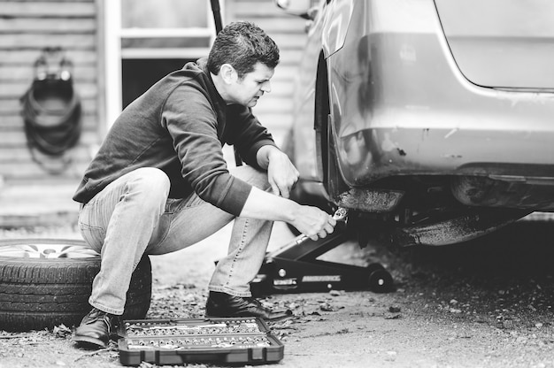 Grayscale shot of a man repairing a wheel