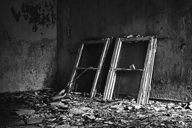 Free photo grayscale shot of window frames placed on a messy floor in an old house