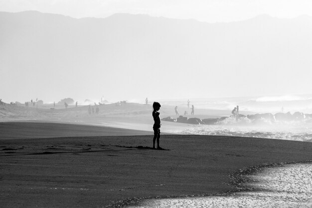 Grayscale shot of a young boy on a sandy seashore near the sea