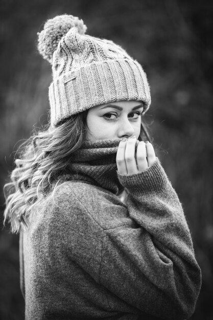 Grayscale shot of young Caucasian woman wearing a gray sweater and winter hat - winter concept