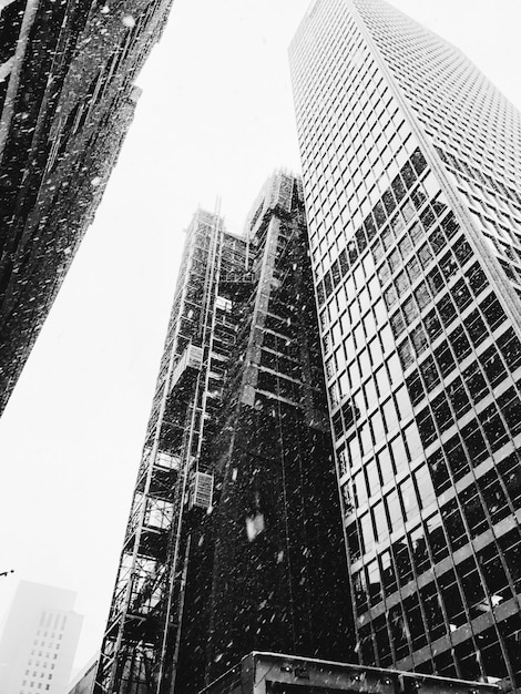 Free photo grayscale vertical low angle shot of high rise buildings while snow