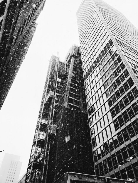 Grayscale vertical low angle shot of high rise buildings while snow