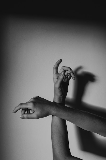 Grayscale vertical shot of graceful hands with a shadow on a wall