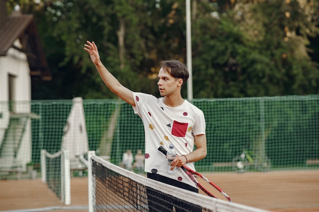 プレーするのに素晴らしい日です！ Tシャツを着た元気な青年。テニスラケットとボールを持っている男。