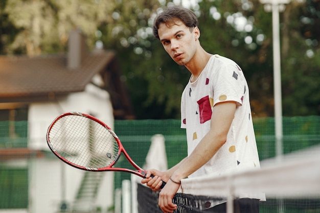 無料写真 プレーするのに素晴らしい日です！ tシャツを着た元気な青年。テニスラケットとボールを持っている男。