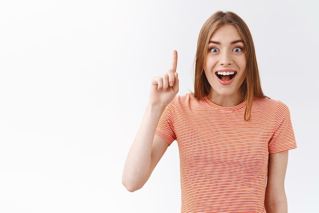 Great idea, girl found solution. Cheerful, amused good-looking woman in striped t-shirt raising one finger, light bulb, eureka gesture, smiling fascinated, suggest something genius, white background