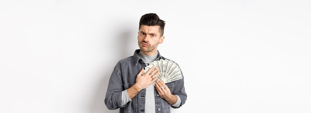 Free photo greedy guy frowning and hugging dollar bills unwilling to share money standing on white background