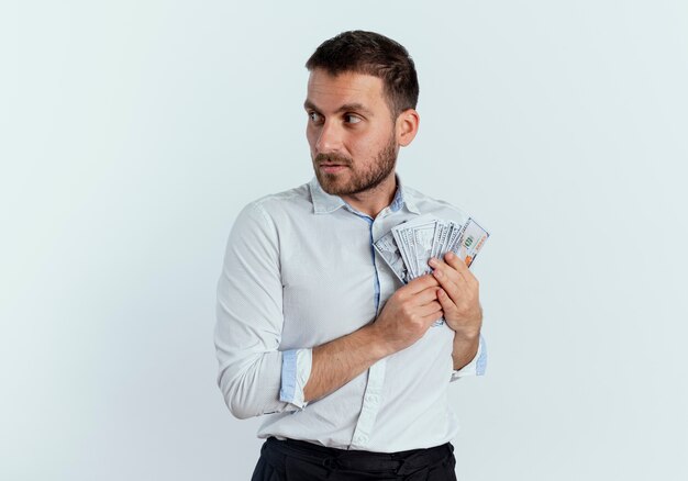 Greedy handsome man holds money looking at side isolated on white wall