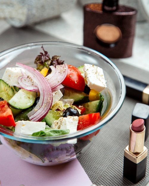 Greek salad bowl next to lipstick and woman perfume