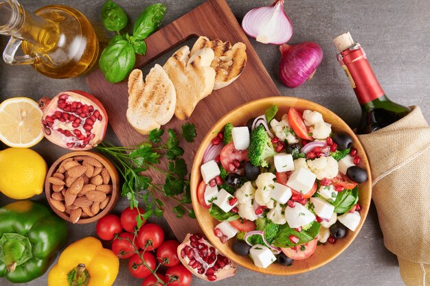 Greek salad or horiatiki with large pieces of tomatoes, cucumbers, onion, feta cheese and olives in white bowl isolated top view. Village salad with diced mozzarella, arugula, parsley and olive oil