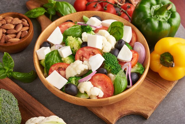 Greek salad or horiatiki with large pieces of tomatoes, cucumbers, onion, feta cheese and olives in white bowl isolated top view. Village salad with diced mozzarella, arugula, parsley and olive oil