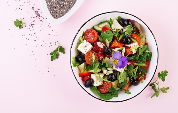 Греческий салат с огурцом, помидорами, сладким перцем, листьями салата, зеленым луком, сыром фета и оливками с оливковым маслом. Здоровая пища. Вид сверху