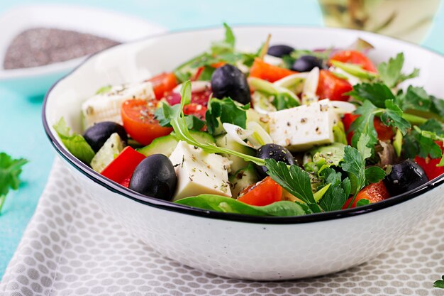 Греческий салат с огурцом, помидорами, сладким перцем, листьями салата, зеленым луком, сыром фета и оливками с оливковым маслом. Здоровая пища.