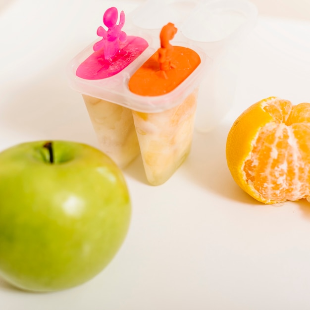 Green apple; orange and popsicle mold on desk